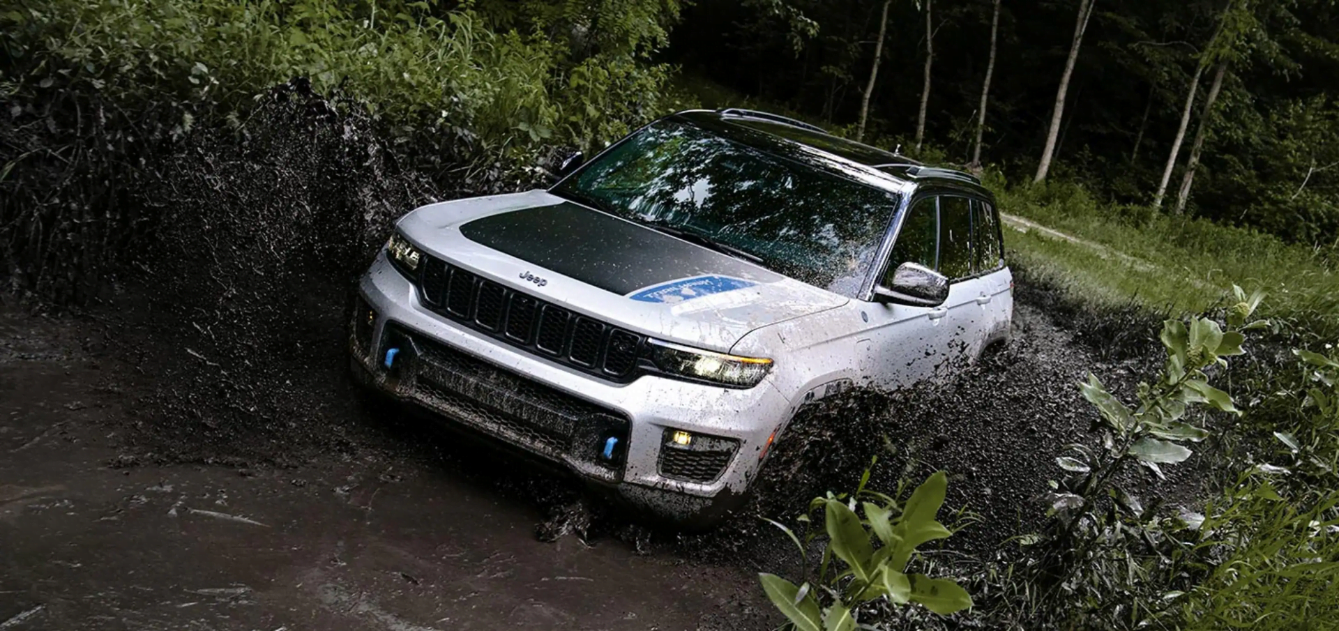 A 2023 Jeep Grand Cherokee, one of the Trail Rated Jeep models, fording water in the forest
