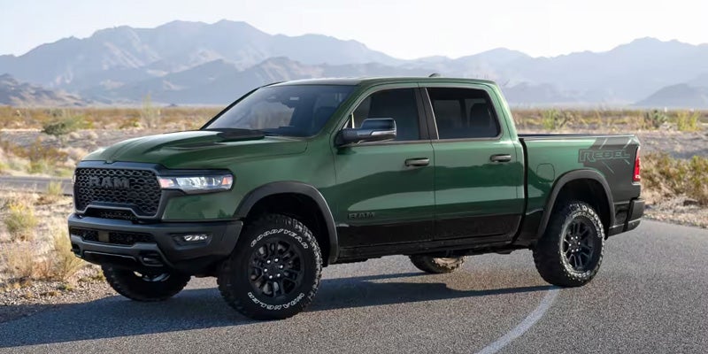 Green RAM pickup truck parked on a scenic road with mountains in the background.